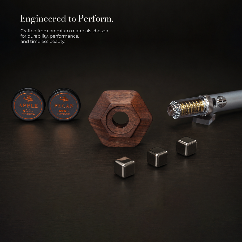 A set of Apple Pegan magnetic fitness pieces arranged on a dark surface, including two round black containers with gold Apple Pegan branding, a central hexagonal wooden weight, three silver metal cubes, and a metallic cylindrical component on a small stand. Text at the top reads 'Engineered to Perform.